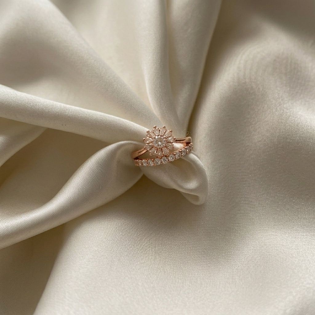 A rose gold ring with a floral sunburst center and a pavé band, displayed on draped cream-colored satin fabric.