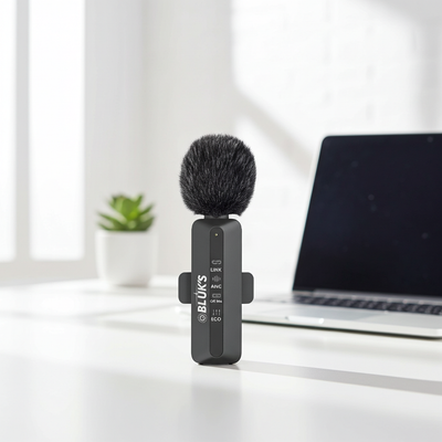 Small black microphone with a fuzzy cover on a white surface with a laptop in the background