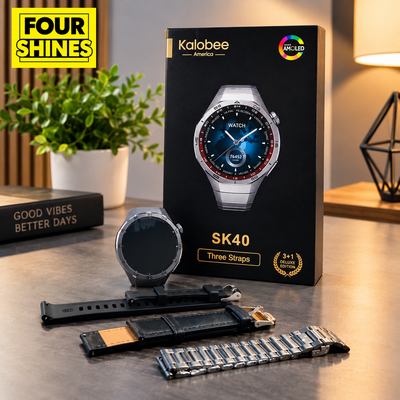 Kalobee Sk40 smartwatch shown with its black retail box, plus three interchangeable straps laid out in front on a tabletop. The watch body is silver-toned, one strap is black leather with a gold-tone buckle, and another is a silver metal link style.