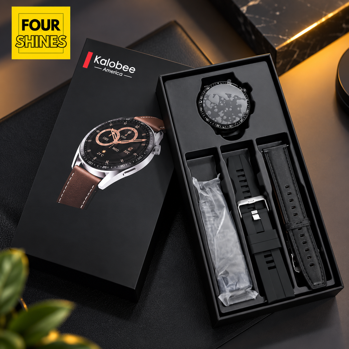 Kalobee smartwatch shown in an open black presentation box with a matching branded box beside it. The watch has a round black dial and a black strap, with a second black strap laid next to it.