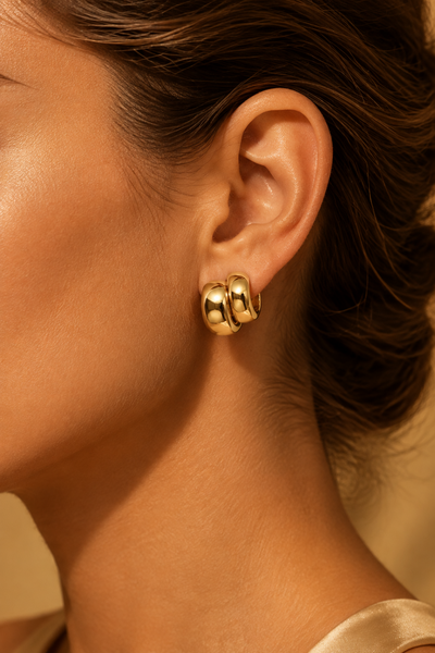 A close-up of a model's ear wearing a pair of chunky, polished gold hoop earrings.