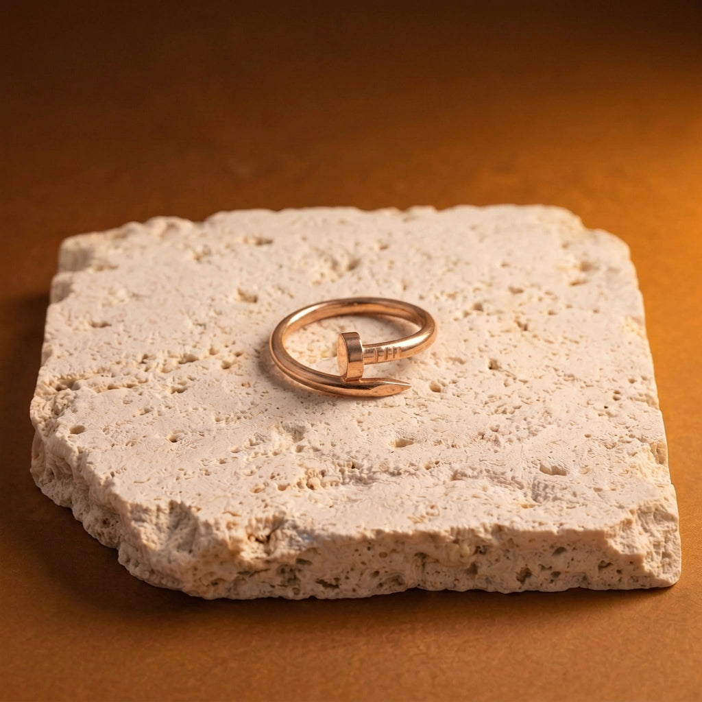 A slim open cuff ring in polished rose gold, displayed on a textured light beige stone slab against a warm brown background.