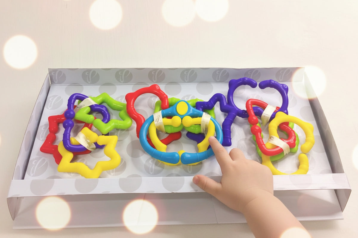 A set of colorful, adjustable rings designed for newborns and toddlers, displayed in an open gift box.