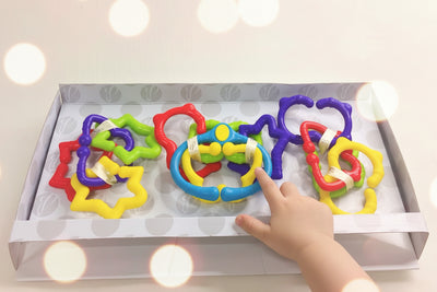 A set of colorful, adjustable rings designed for newborns and toddlers, displayed in an open gift box.