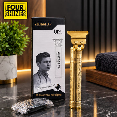 A gold-colored vintage T9 clipper shown next to its black and white retail box on a dark marble countertop, with a small foil-wrapped accessory and a folded dark towel nearby.