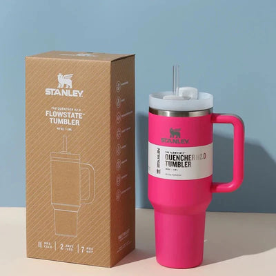 Pink Stanley tumbler with straw and handle next to its packaging on a light blue background