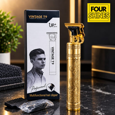 A gold-colored vintage T9 multifunctional hair clipper with dragon engravings stands next to its black and white retail box on a dark marble countertop. A small black comb and plastic-wrapped accessories sit in the foreground, with a blurred indoor setting in the background.