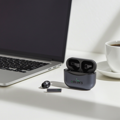 Black wireless earbuds with charging case on a desk next to a laptop and coffee cup.