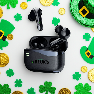Black wireless earbuds with charging case on a St. Patrick's Day-themed background with green hats, gold coins, and shamrocks.