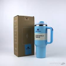Blue travel mug with handle next to a cardboard box on a white background