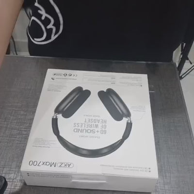 Black headphones with digital display on a wooden surface, next to their packaging box labeled 'AKZ Max700'.