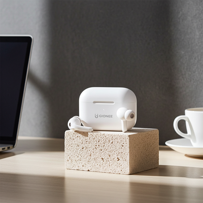 White Gionee earbuds in a charging case on a wooden block with a laptop and cup in the background.